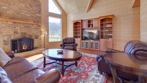 A cozy living room with a stone fireplace, leather furniture, and a large TV.