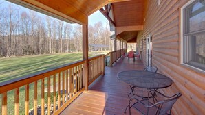 A covered wooden deck with a table and chairs, overlooking a grassy area with trees.
