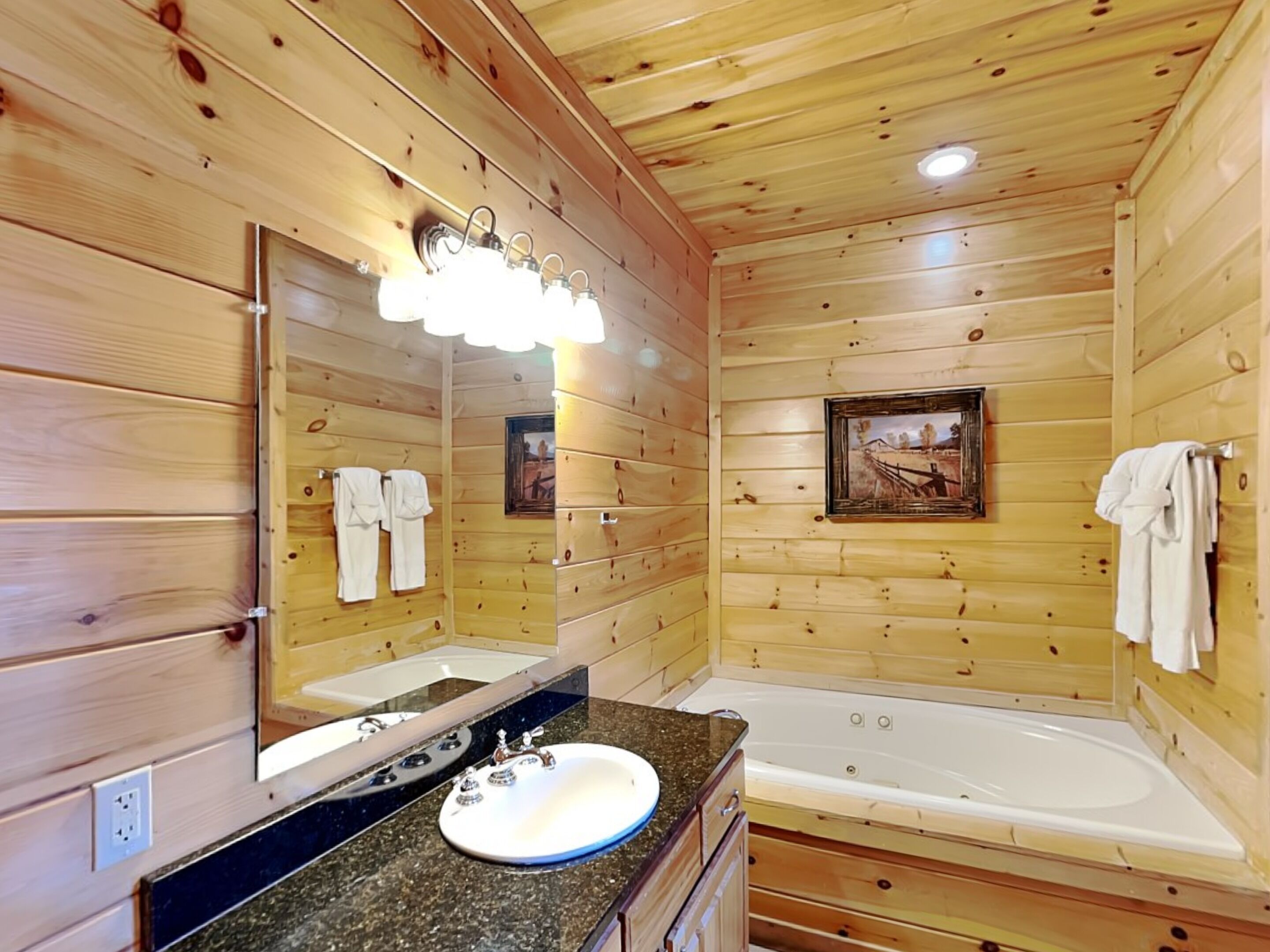 A wooden cabin bathroom with a large mirror, a sink, a bathtub, and towels hanging on the wall.