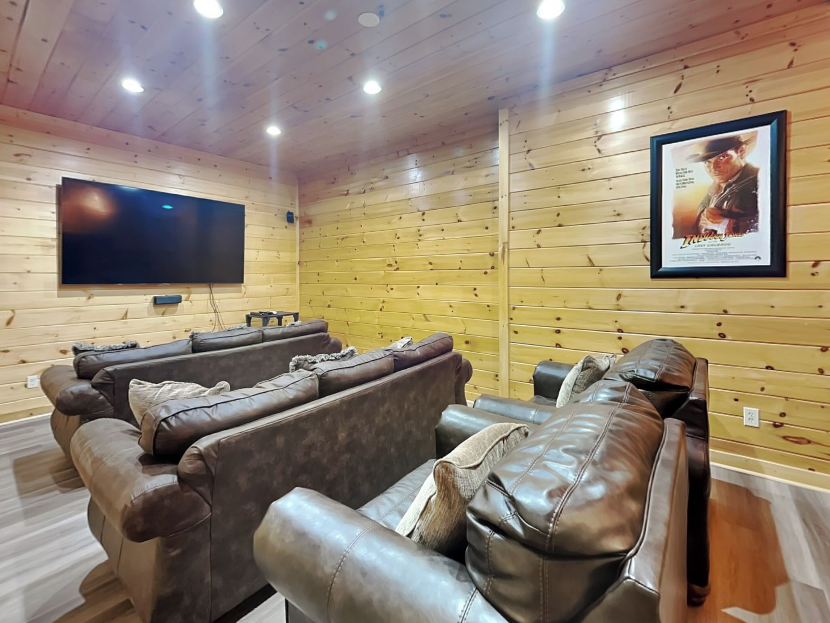Ein gemütliches Zimmer mit Holzwänden und -decke, einem großen Flachbildfernseher an der Wand und einer Sitzecke mit Ledersofas und einem kleinen Tisch.