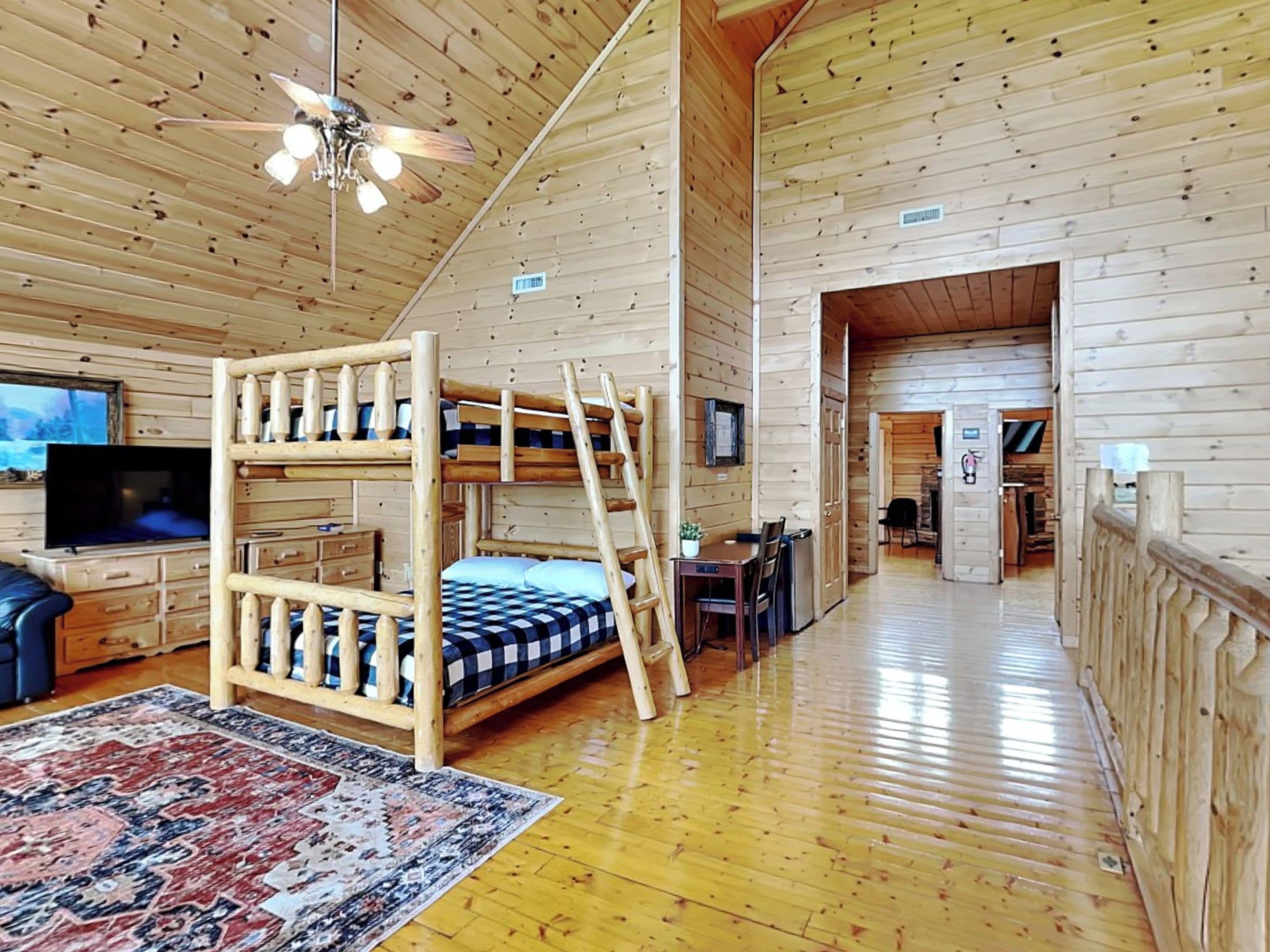 Interior de una cabaña de madera con una cama litera, televisor, escritorio y comedor.