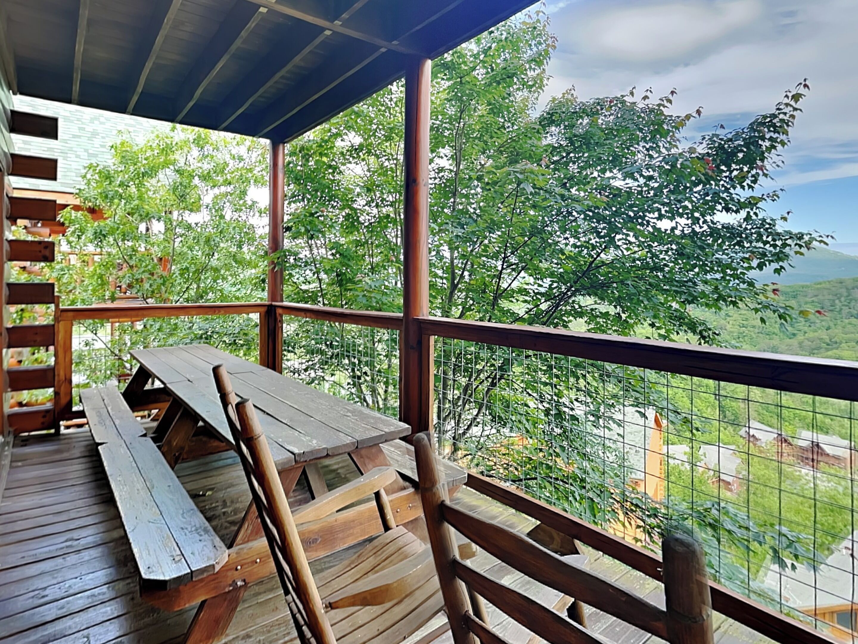 A wooden deck with picnic tables and a metal railing overlooking a lush green landscape.