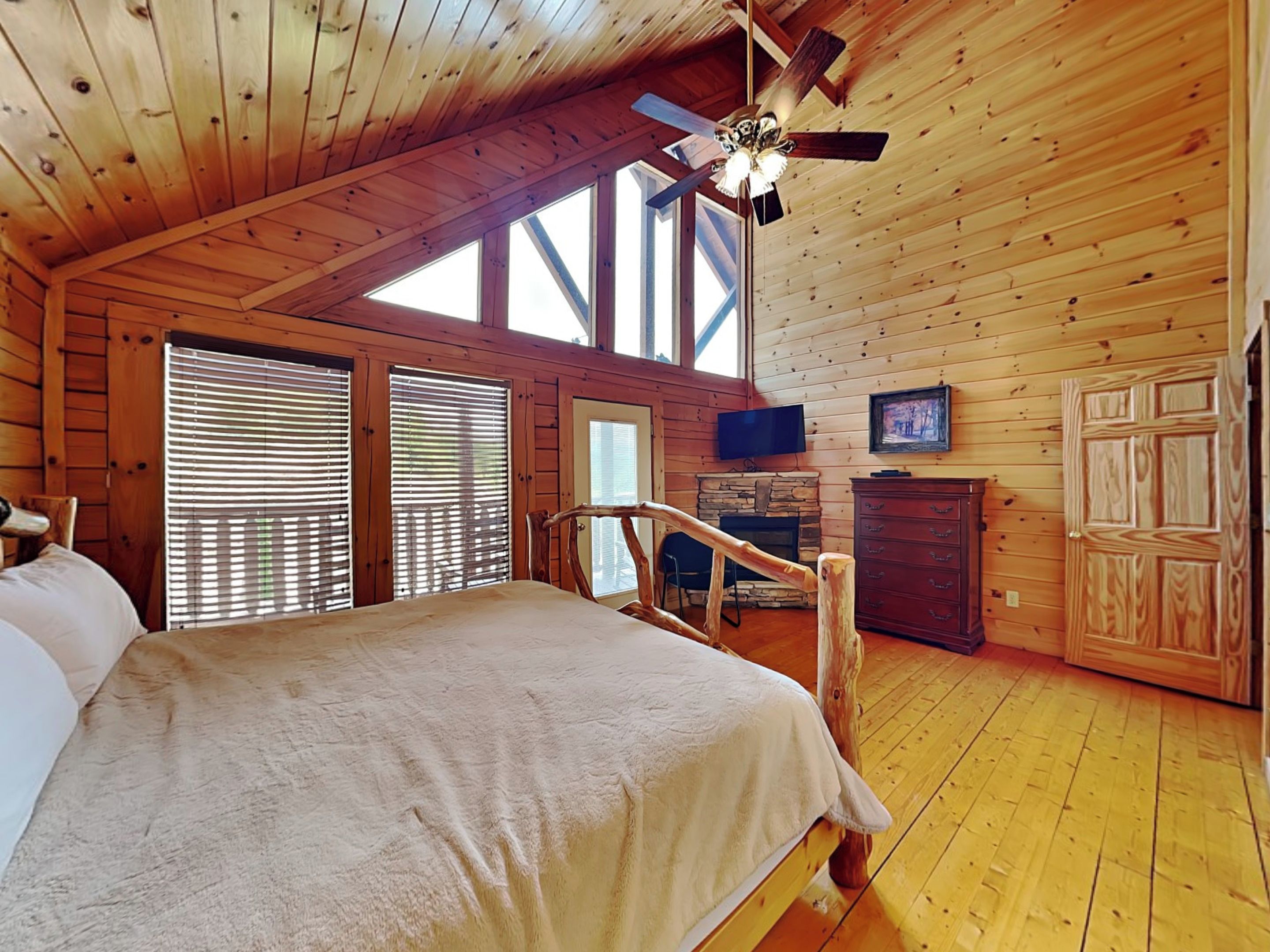 Ein gemütliches Schlafzimmer in einer Blockhütte mit Bett, Holzwänden, Kamin, Fernseher und Deckenventilator.