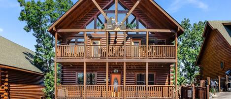 A two-story log cabin with a balcony, wooden railings, and a clear sky.