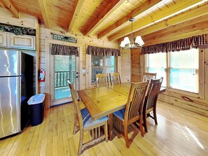 A wooden cabin interior with a dining table, chairs, a refrigerator, and a trash bin. - Peyton's Hideaway by Jackson Mountain Rentals (Gatlinburg)