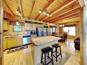 A wooden cabin interior with a kitchen, dining area, and a bar area. - Peyton's Hideaway by Jackson Mountain Rentals (Gatlinburg)