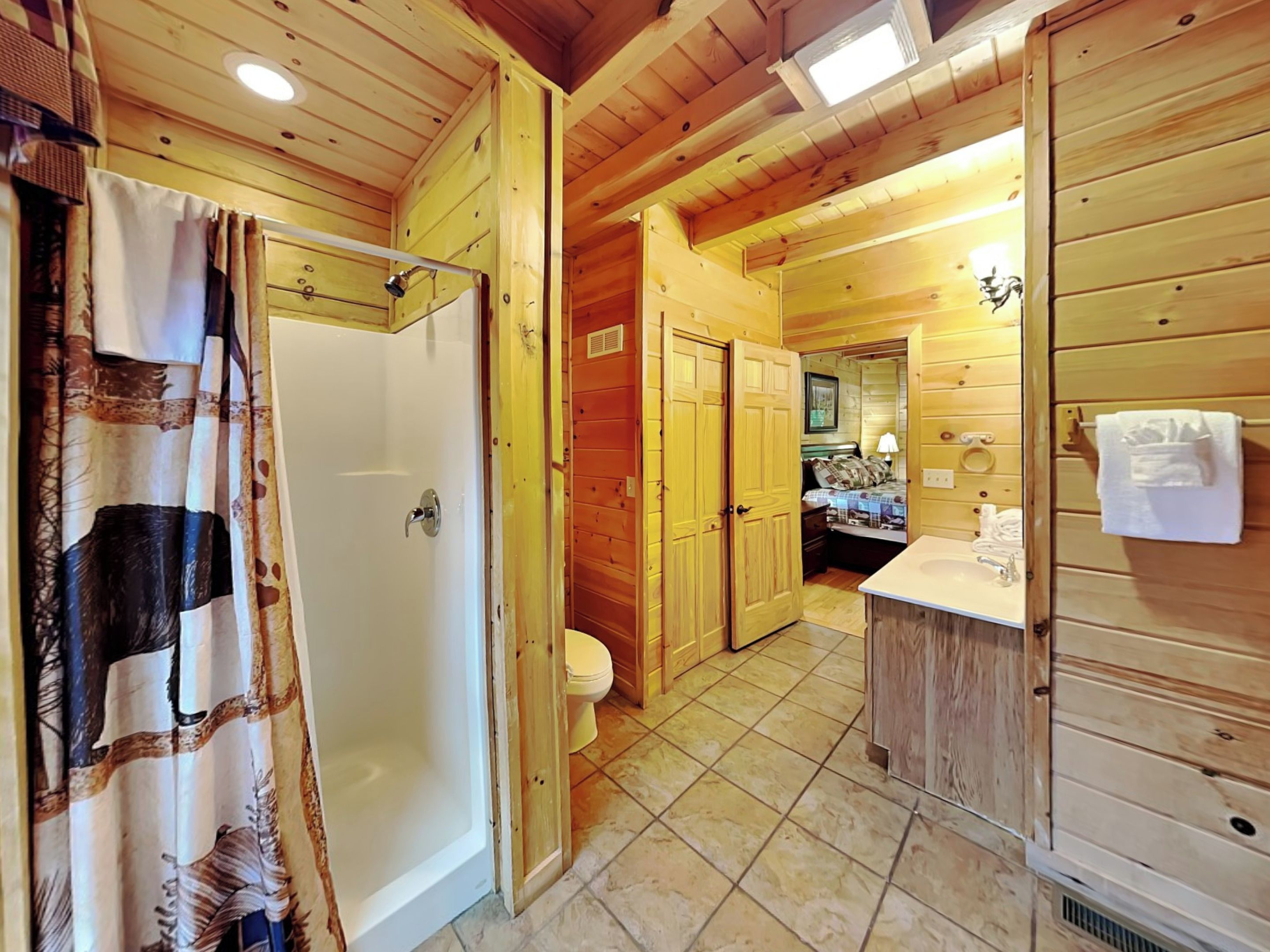 Baño de cabaña de madera con ducha, inodoro y lavamanos.
