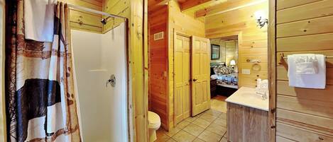 Baño de cabaña de madera con ducha, inodoro y lavamanos.