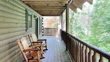 A wooden porch with a railing, wooden rocking chairs, and a view of a forest.