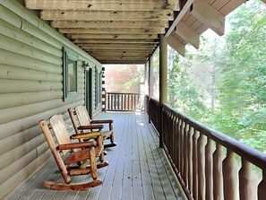 A wooden porch with a railing, wooden rocking chairs, and a view of a forest. - Peyton's Hideaway by Jackson Mountain Rentals (Gatlinburg)