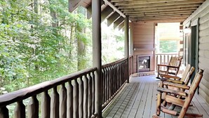 Eine Holzterrasse mit Geländer, Kamin und mehreren Schaukelstühlen.