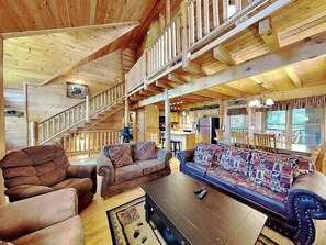 A spacious living area with a wooden staircase, a sofa set, a coffee table, and a kitchen in the background. - Peyton's Hideaway by Jackson Mountain Rentals (Gatlinburg)
