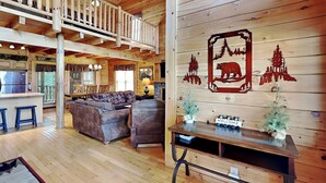 Geräumiges Ferienhaus-Interieur mit Holzvertäfelung, einem Essbereich, einem Wohnzimmer mit Sofa und Sesseln sowie einer Holzbalkendecke und einem Balkon.