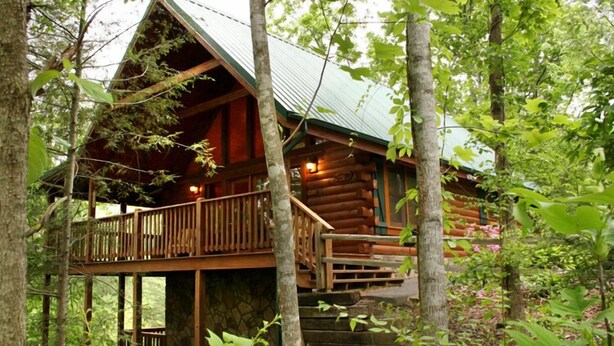 A log cabin with a wooden deck and stone foundation, surrounded by trees. - Running Bear by Jackson Mountain Rentals (Gatlinburg)
