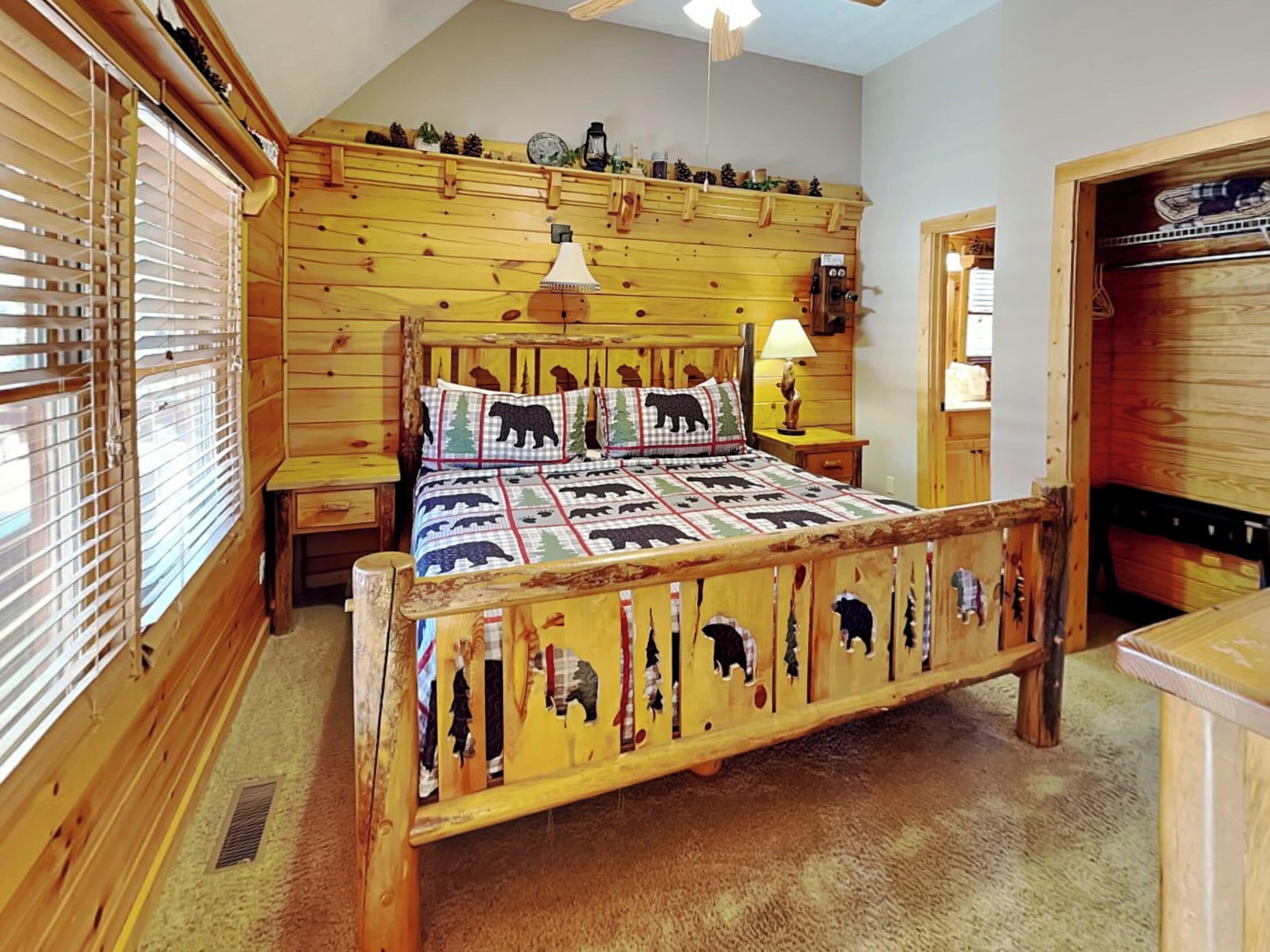 A wooden bedroom with a bed featuring a bear-themed quilt, wooden headboard, and a nightstand with a lamp.