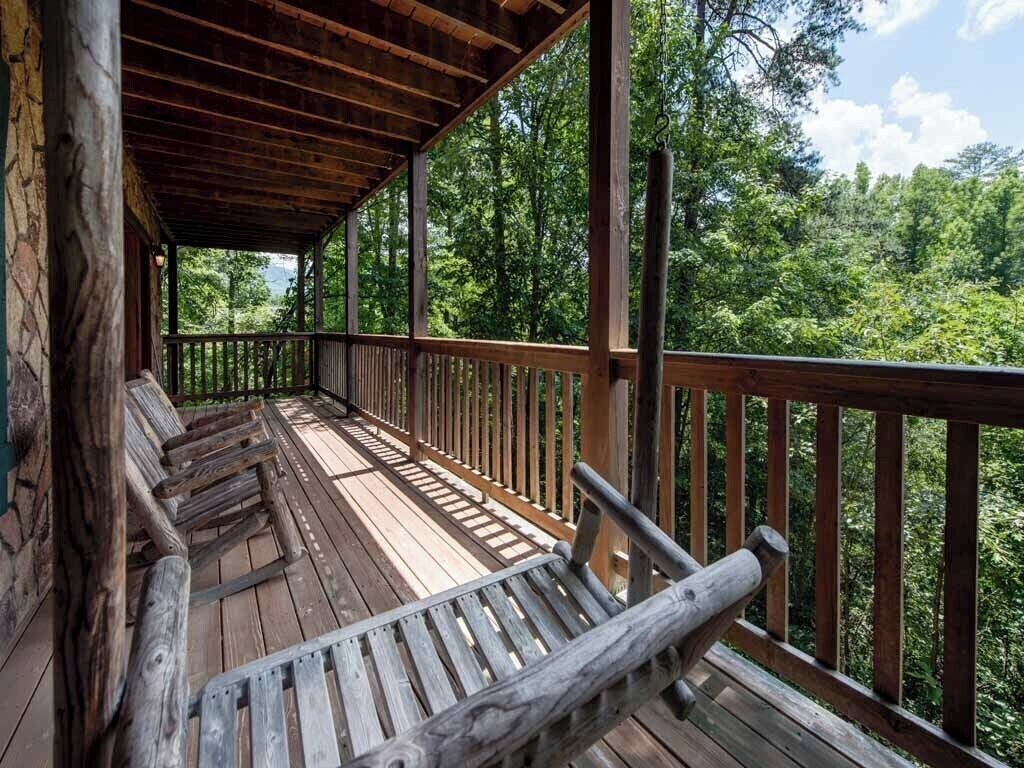 A wooden deck with benches, surrounded by a railing, overlooking a forested area.