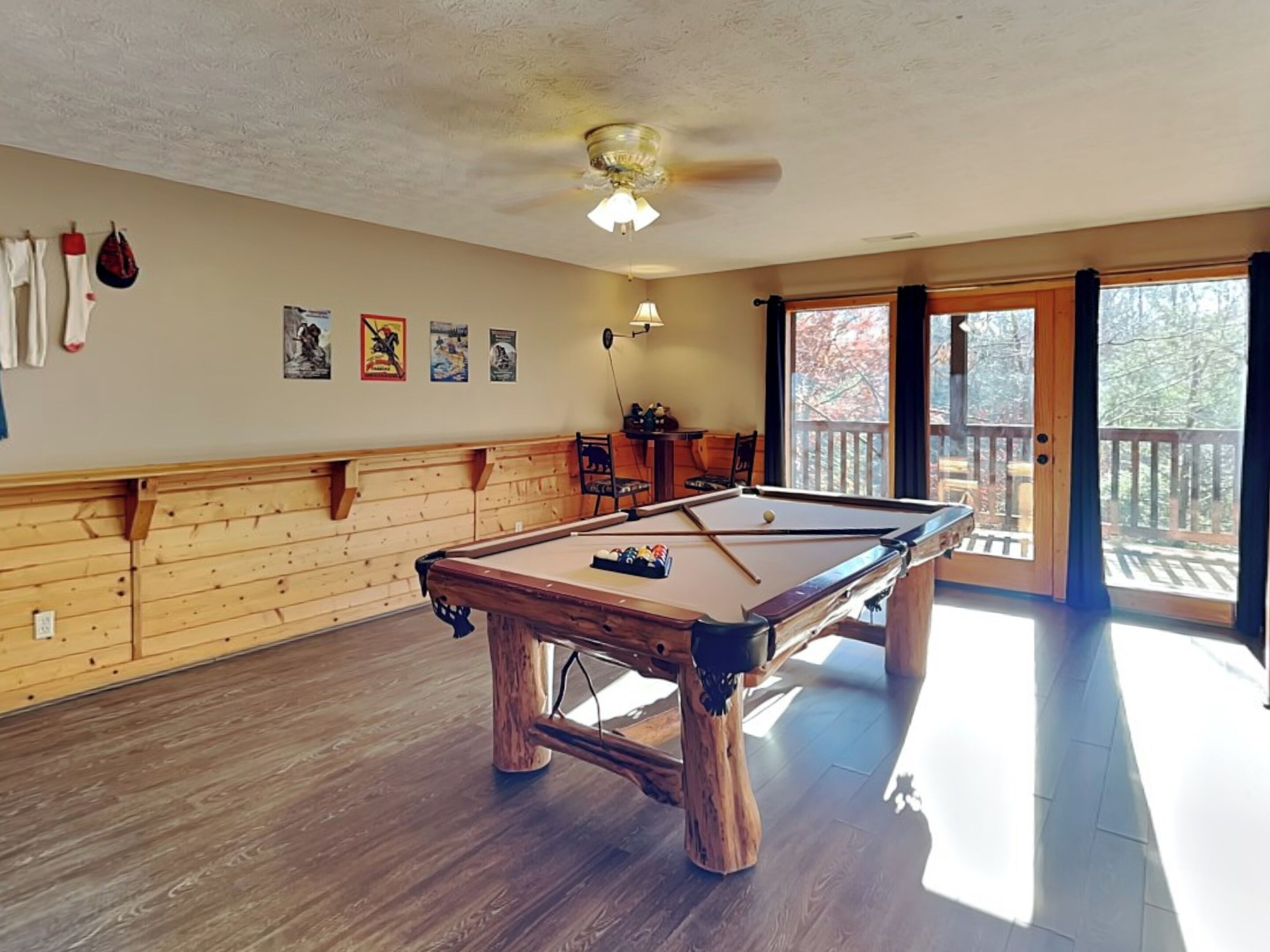 A pool table in a room with wooden paneling, a ceiling fan, and a view through a glass door.