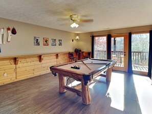 A pool table in a room with wooden paneling, a ceiling fan, and a view through a glass door. - Running Bear by Jackson Mountain Rentals (Gatlinburg)