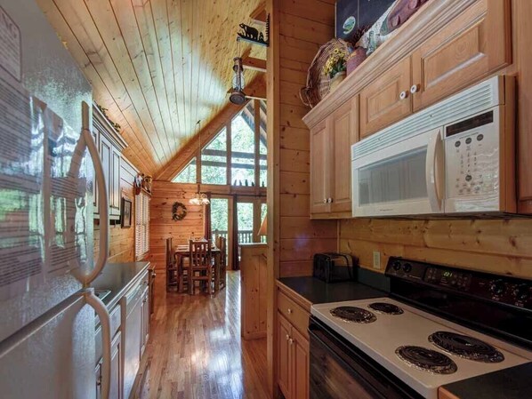 A wooden cabin interior with a kitchen featuring a stove, microwave, and wooden cabinets. - Running Bear by Jackson Mountain Rentals (Gatlinburg)