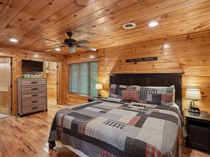 A wooden-paneled bedroom with a bed, a dresser, a television, and a ceiling fan. - Parkside Lodge by Jackson Mountain Rentals (Sevierville)