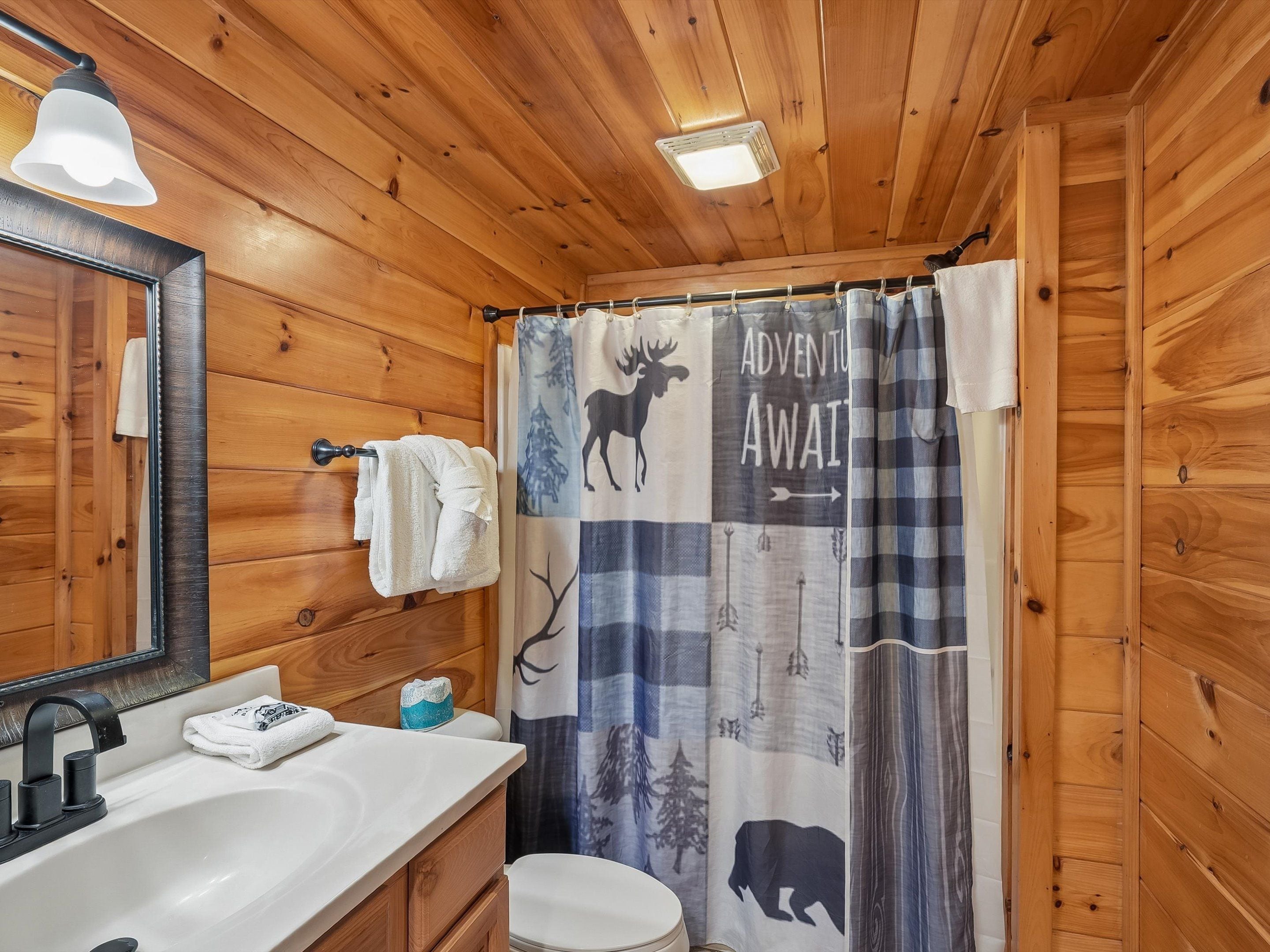 A wooden cabin bathroom with a sink, mirror, towel rack, and a shower curtain with a wildlife theme.
