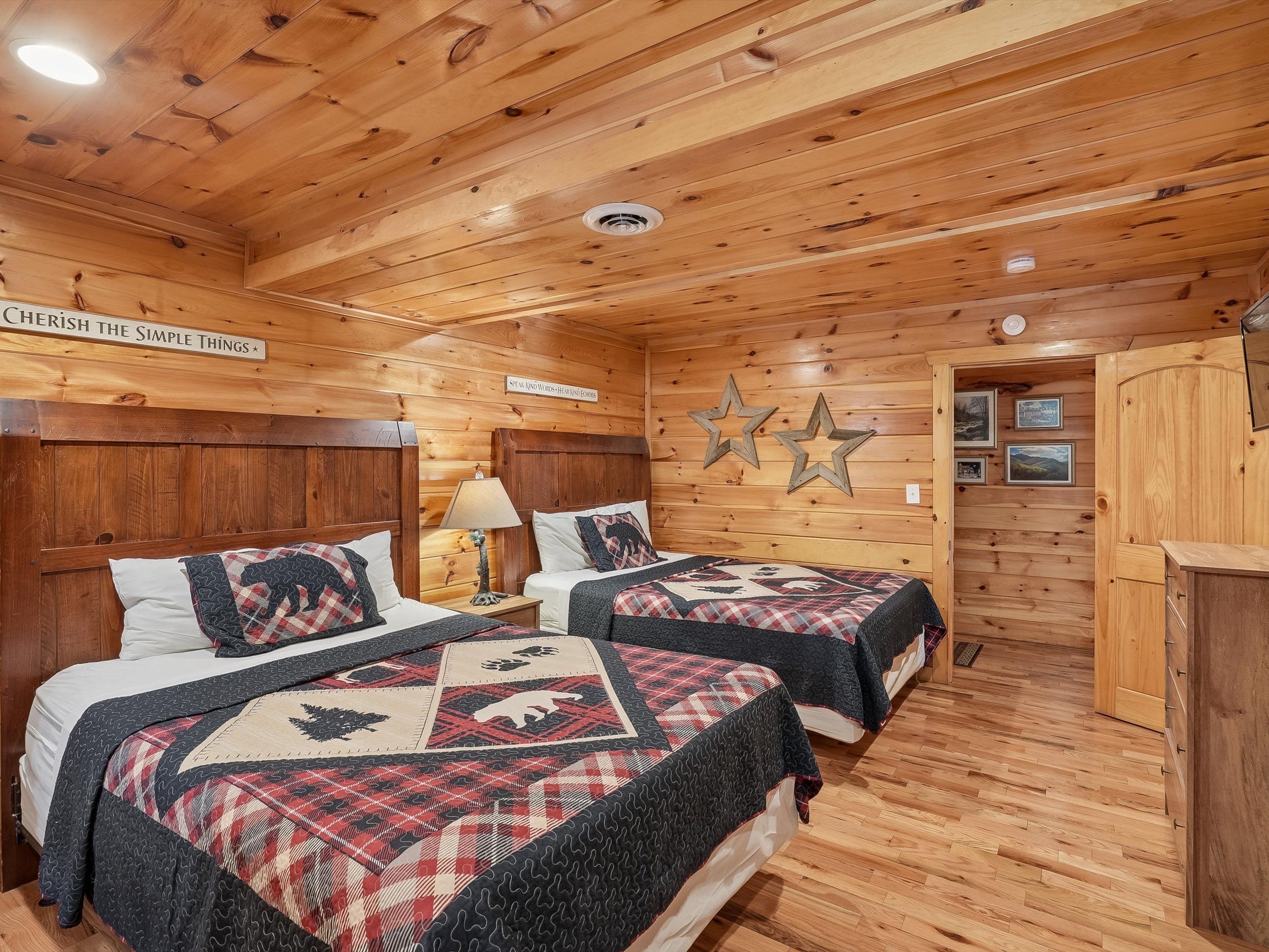 A cozy cabin-style bedroom with two beds, wooden walls, and a ceiling with exposed beams.