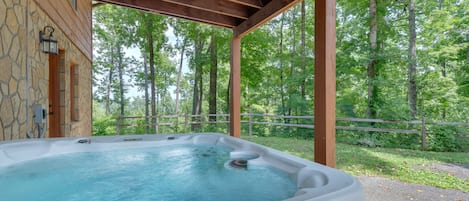 Un bain à remous sous une pergola en bois, avec un mur en pierre et une clôture en bois, situé dans un espace boisé.