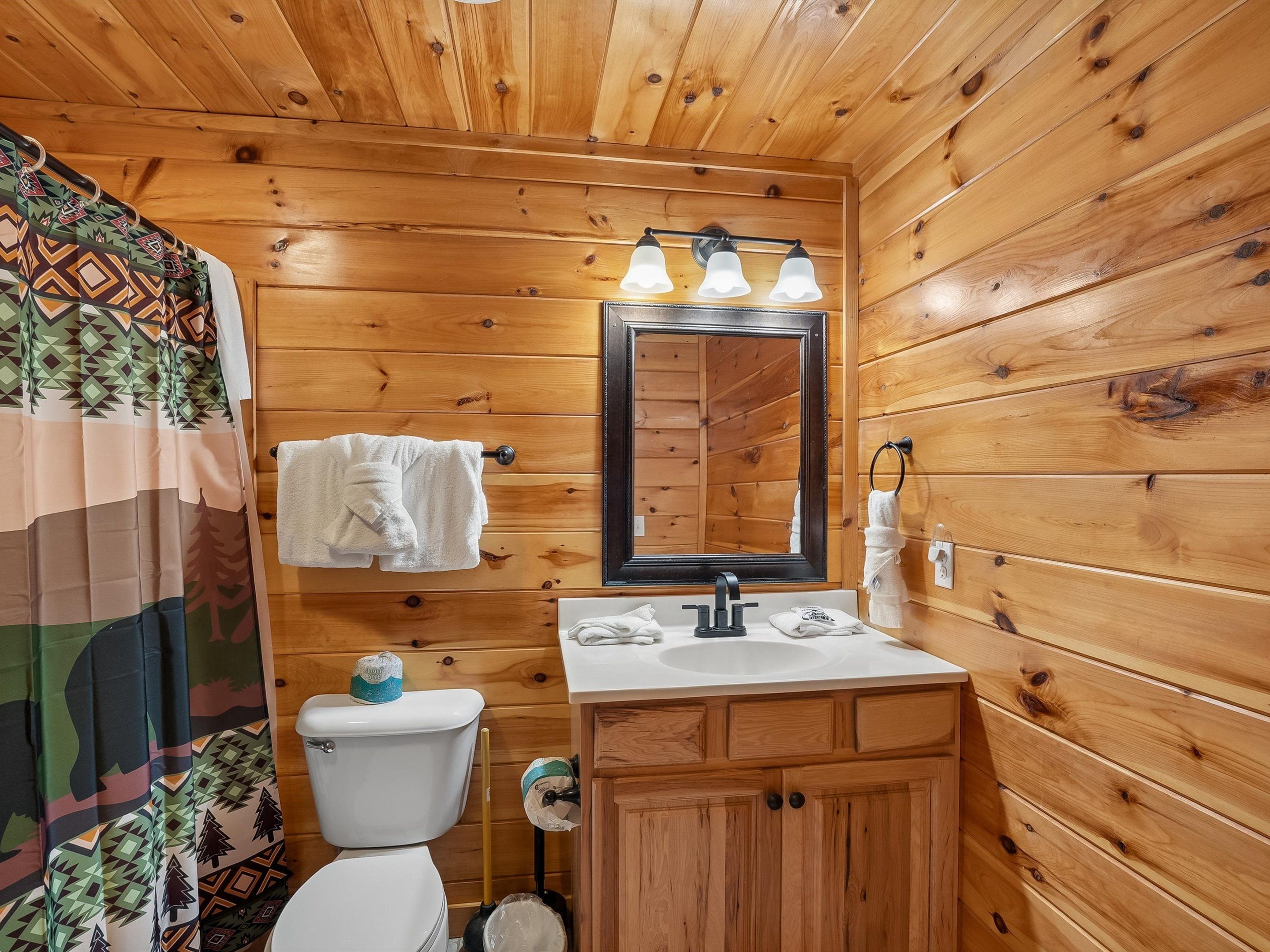 A wooden-paneled bathroom with a toilet, sink, mirror, and towel rack.