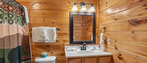 A wooden-paneled bathroom with a toilet, sink, mirror, and towel rack.