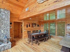 A wooden interior with a stone wall, wooden ceiling, and a dining area with benches and chairs. - Parkside Lodge by Jackson Mountain Rentals (Sevierville)