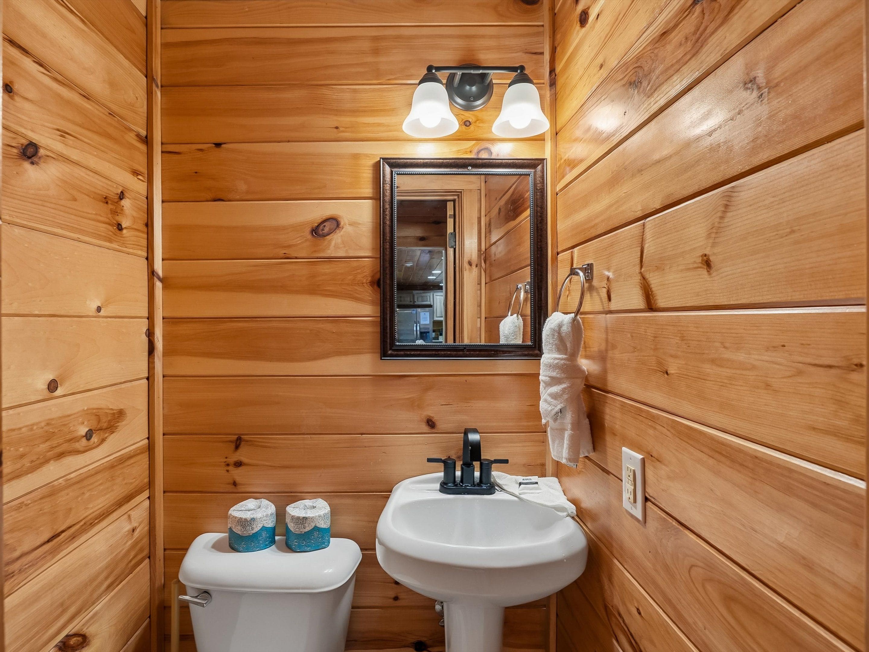 Une salle de bain aux murs lambrissés, équipée de toilettes, d’un lavabo et d’un miroir.