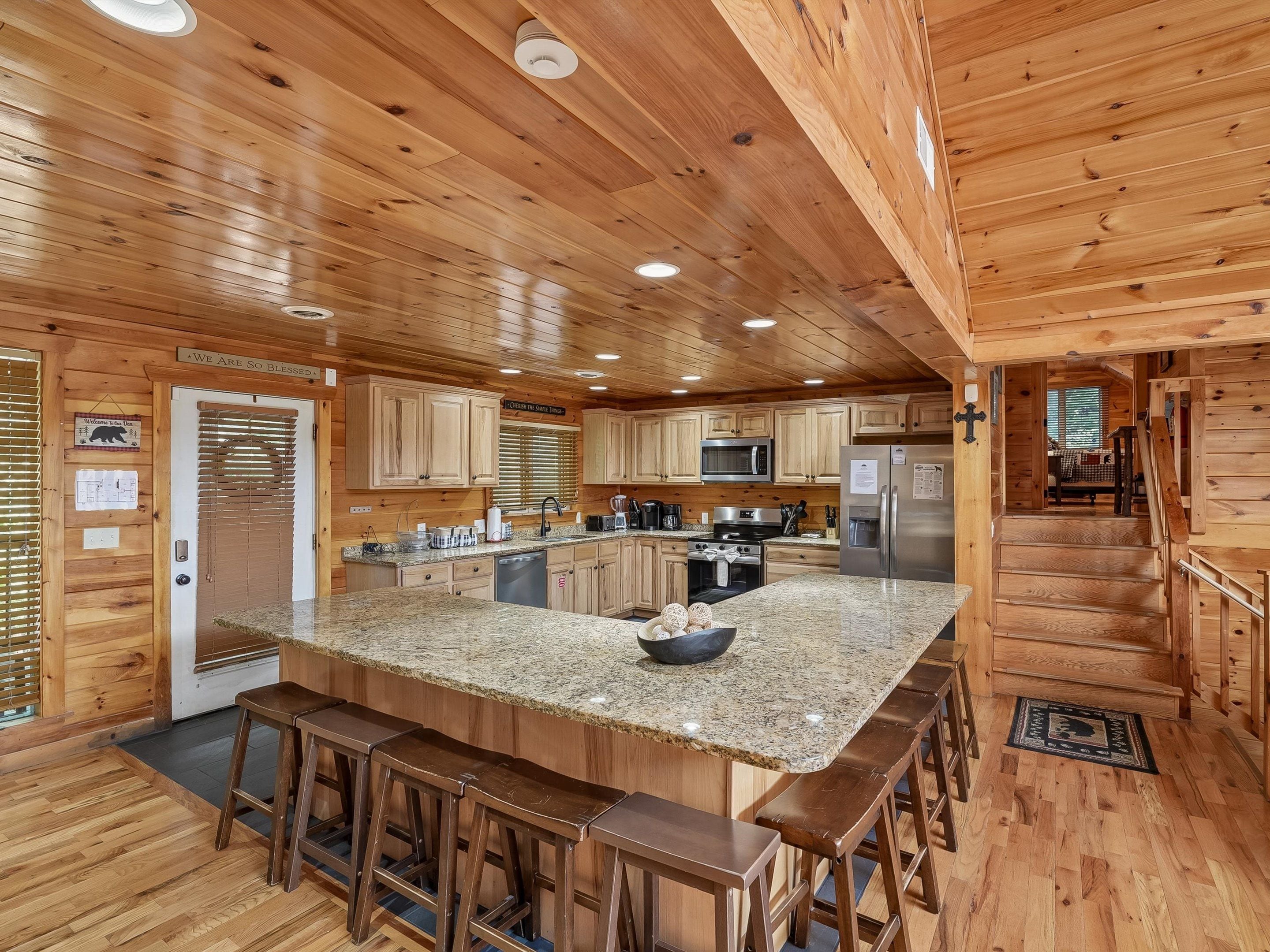 A wooden cabin interior with a kitchen featuring granite countertops, wooden bar stools, and a central island.