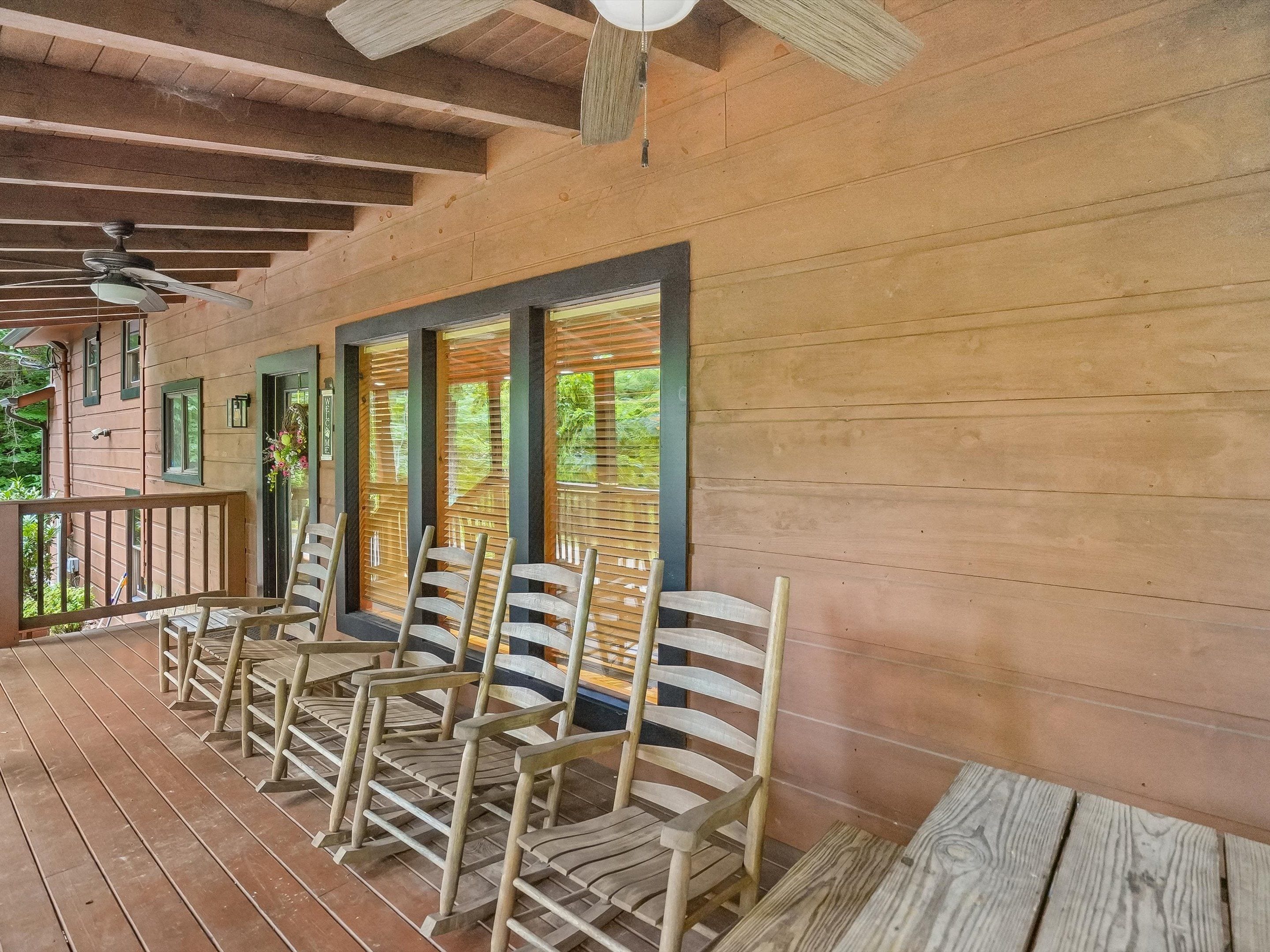 A covered outdoor seating area with wooden chairs and a ceiling fan.