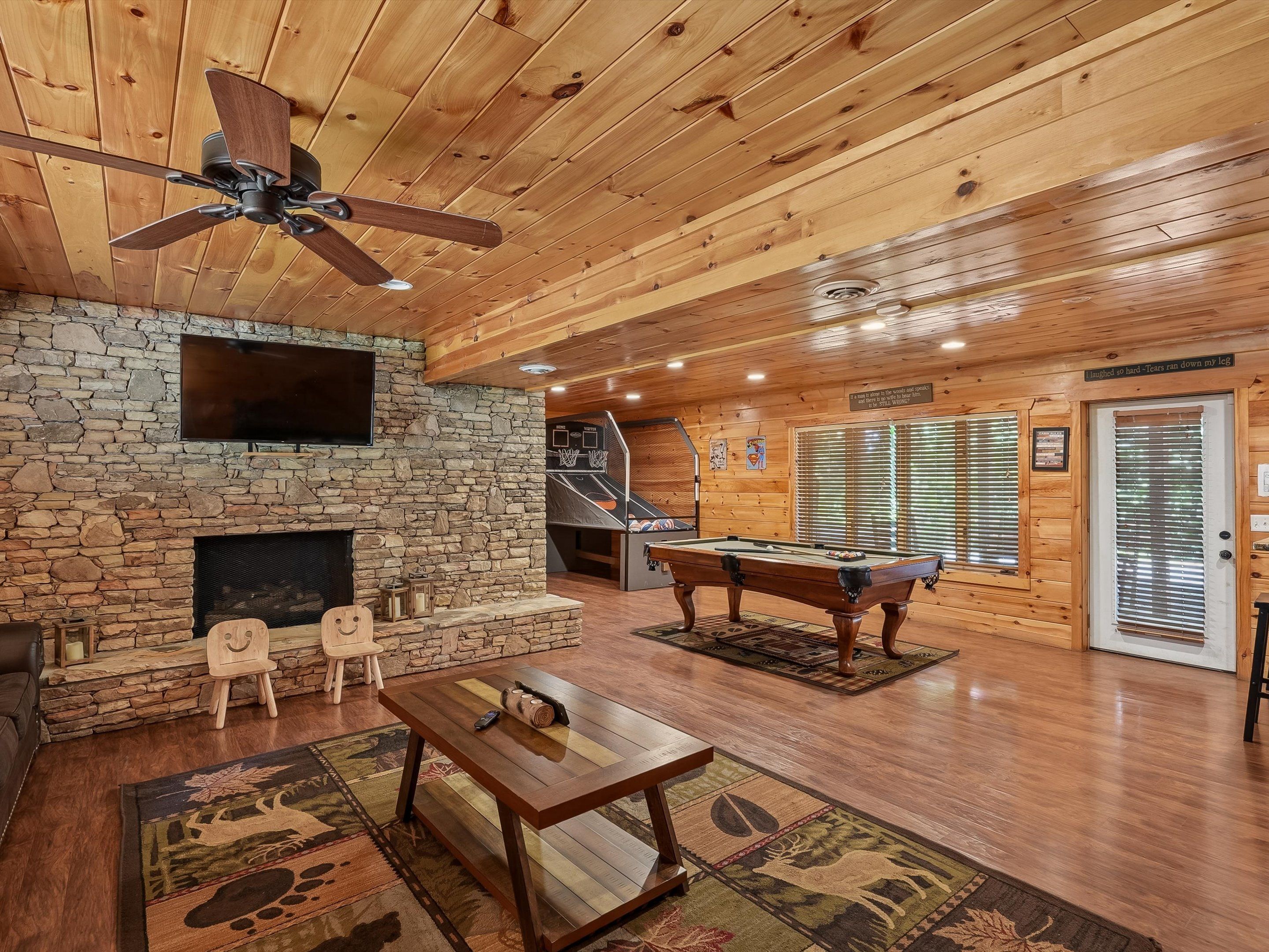 A wooden interior with a stone fireplace, a pool table, and a ceiling fan.