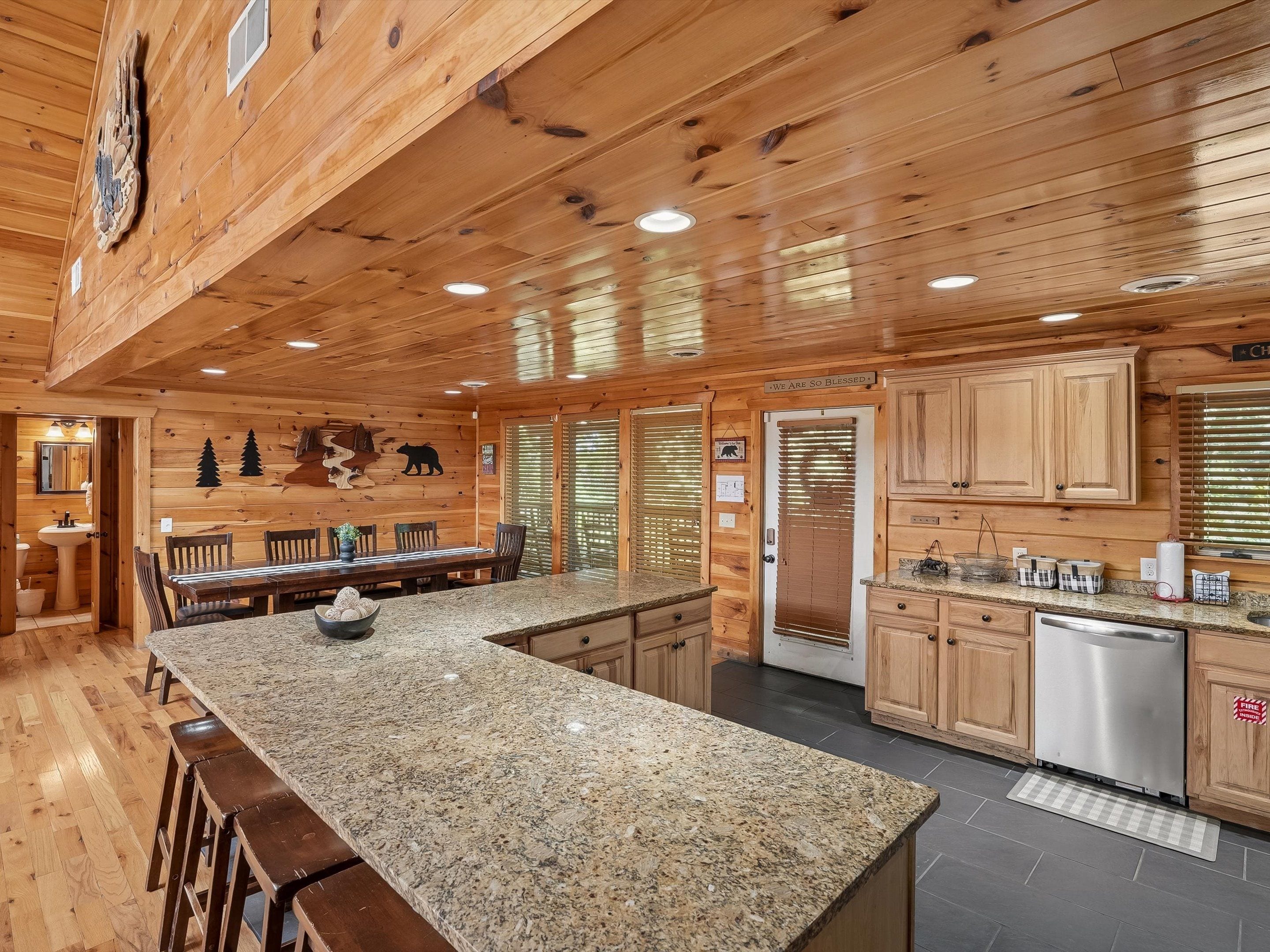 A wooden cabin interior with a granite kitchen island, wooden cabinets, and a stainless steel dishwasher.