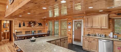 A wooden cabin interior with a granite kitchen island, wooden cabinets, and a stainless steel dishwasher.