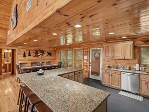 A wooden cabin interior with a granite kitchen island, wooden cabinets, and a stainless steel dishwasher. - Parkside Lodge by Jackson Mountain Rentals (Sevierville)