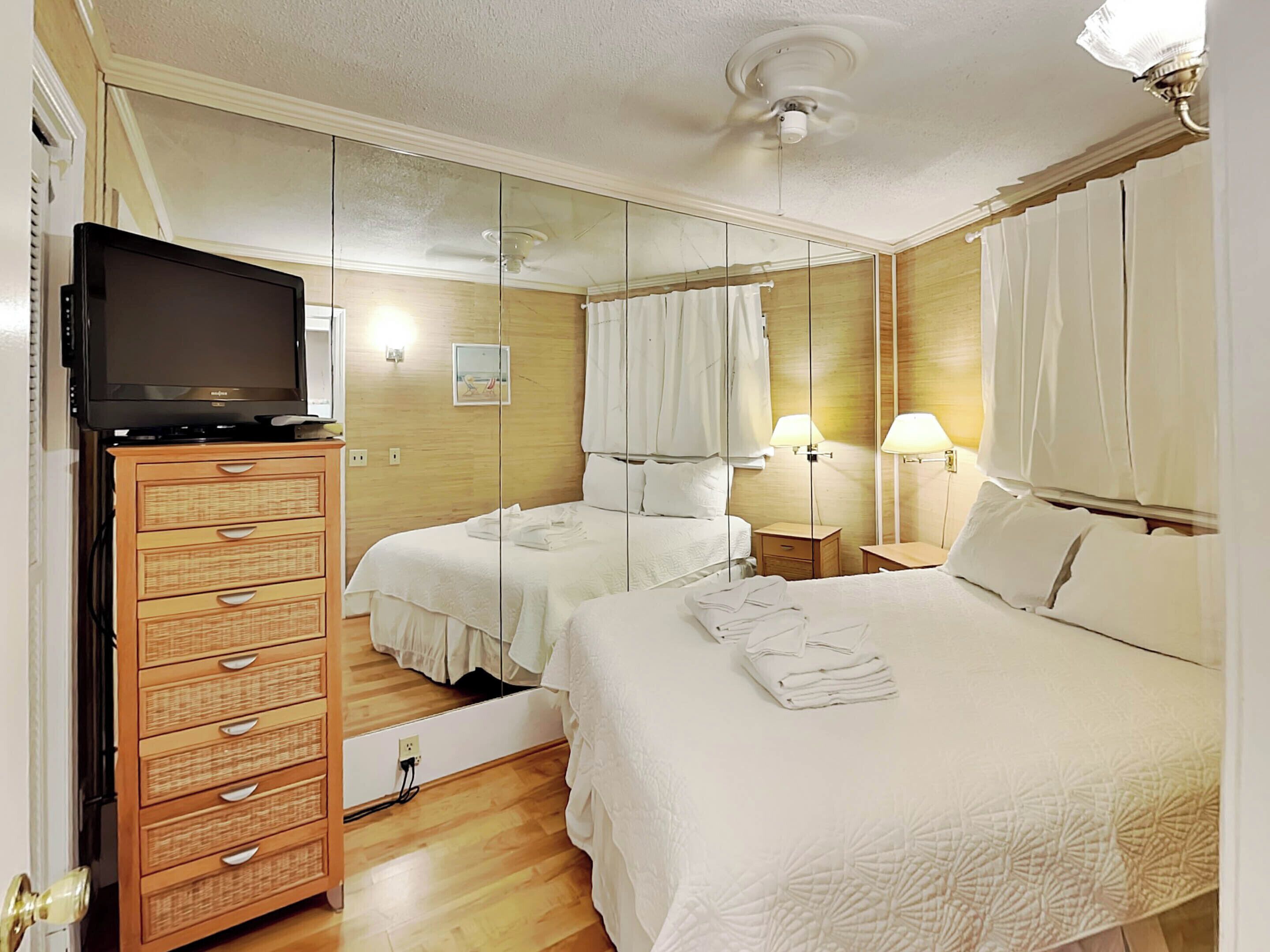 A hotel room with a bed, a TV on a wooden cabinet, a mirror, and two bedside lamps.