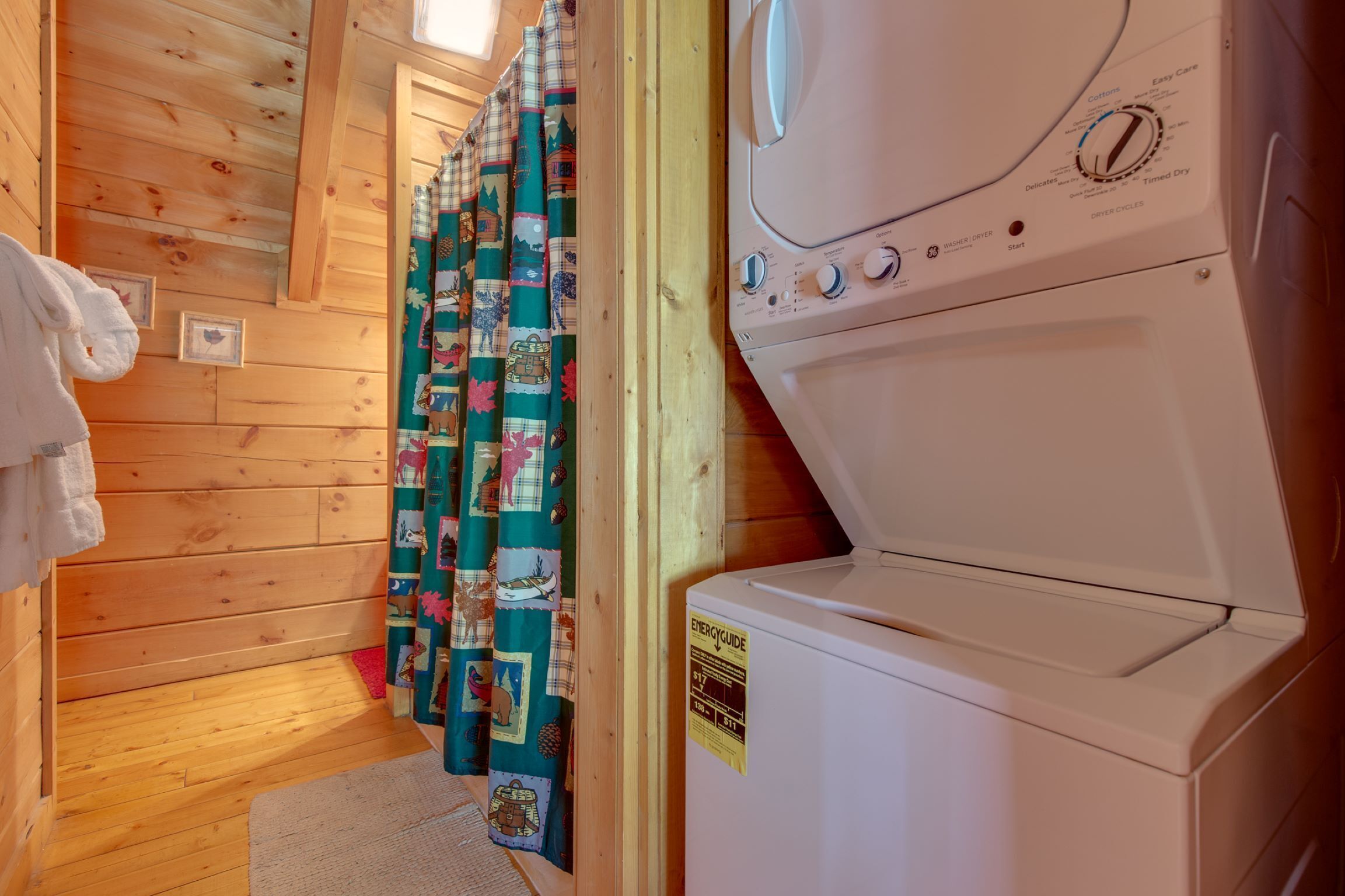 Un cuarto de lavandería con una lavadora blanca, paredes de madera y una cortina con diversos diseños.