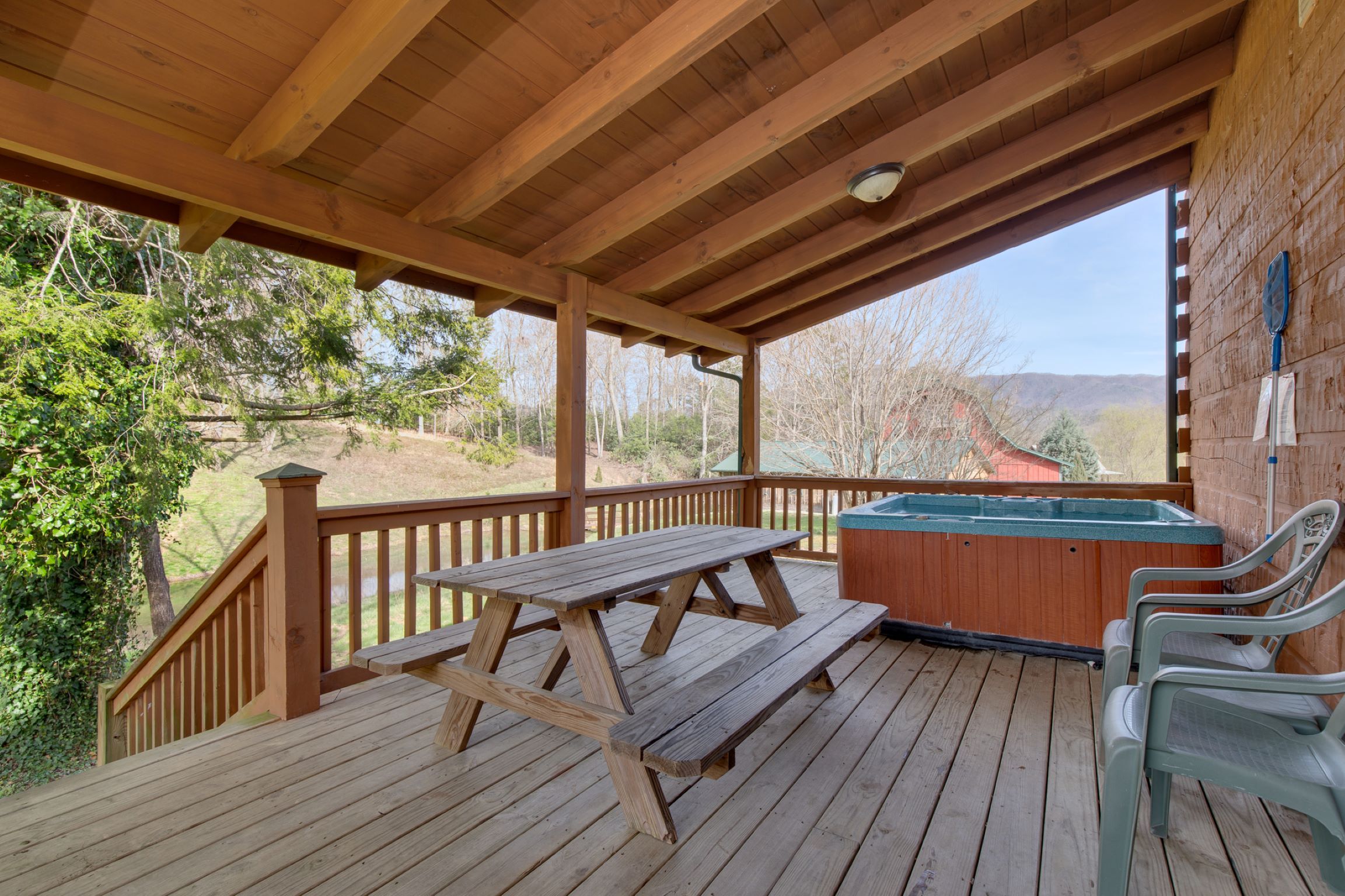 A wooden deck with a picnic table and chairs, a hot tub, and a view of the surrounding landscape.