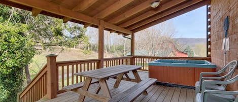 A wooden deck with a picnic table and chairs, a hot tub, and a view of the surrounding landscape.