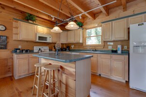 Una cocina amplia con armarios de madera, una isla central con taburetes, un microondas y un refrigerador.