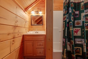 A wooden cabin bathroom with a sink, mirror, and shower curtain.