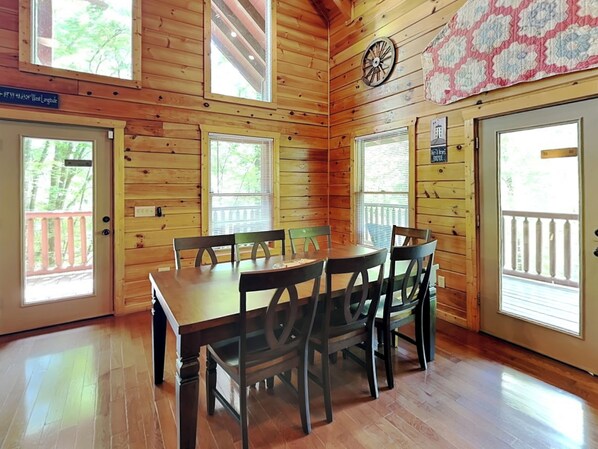 A wooden cabin with a dining table and chairs, large windows, and a clock on the wall. - Take It Easy by Jackson Mountain Rentals (Pigeon Forge)