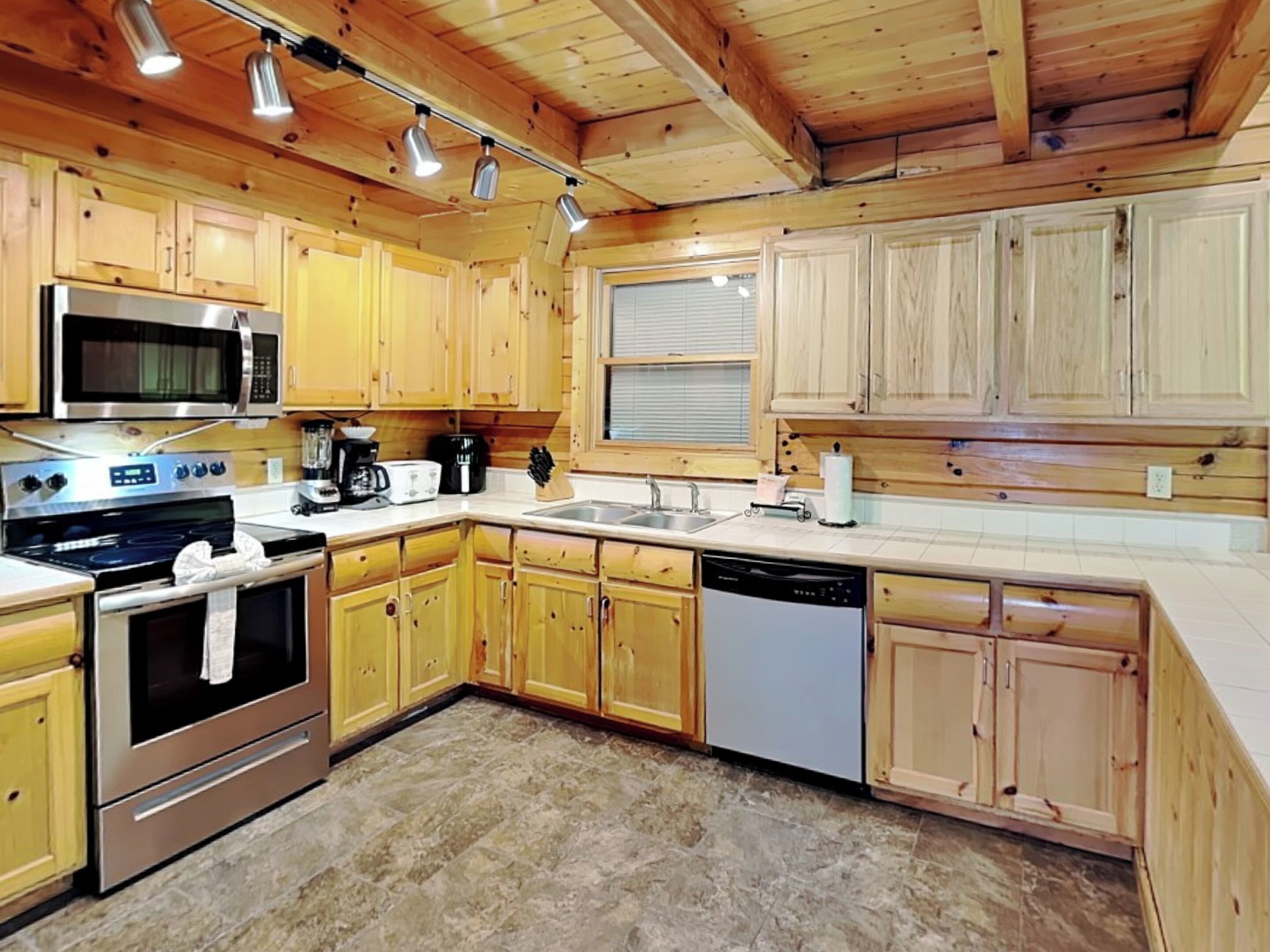 A kitchen with wooden cabinets, a microwave, stove, dishwasher, and a window with blinds.