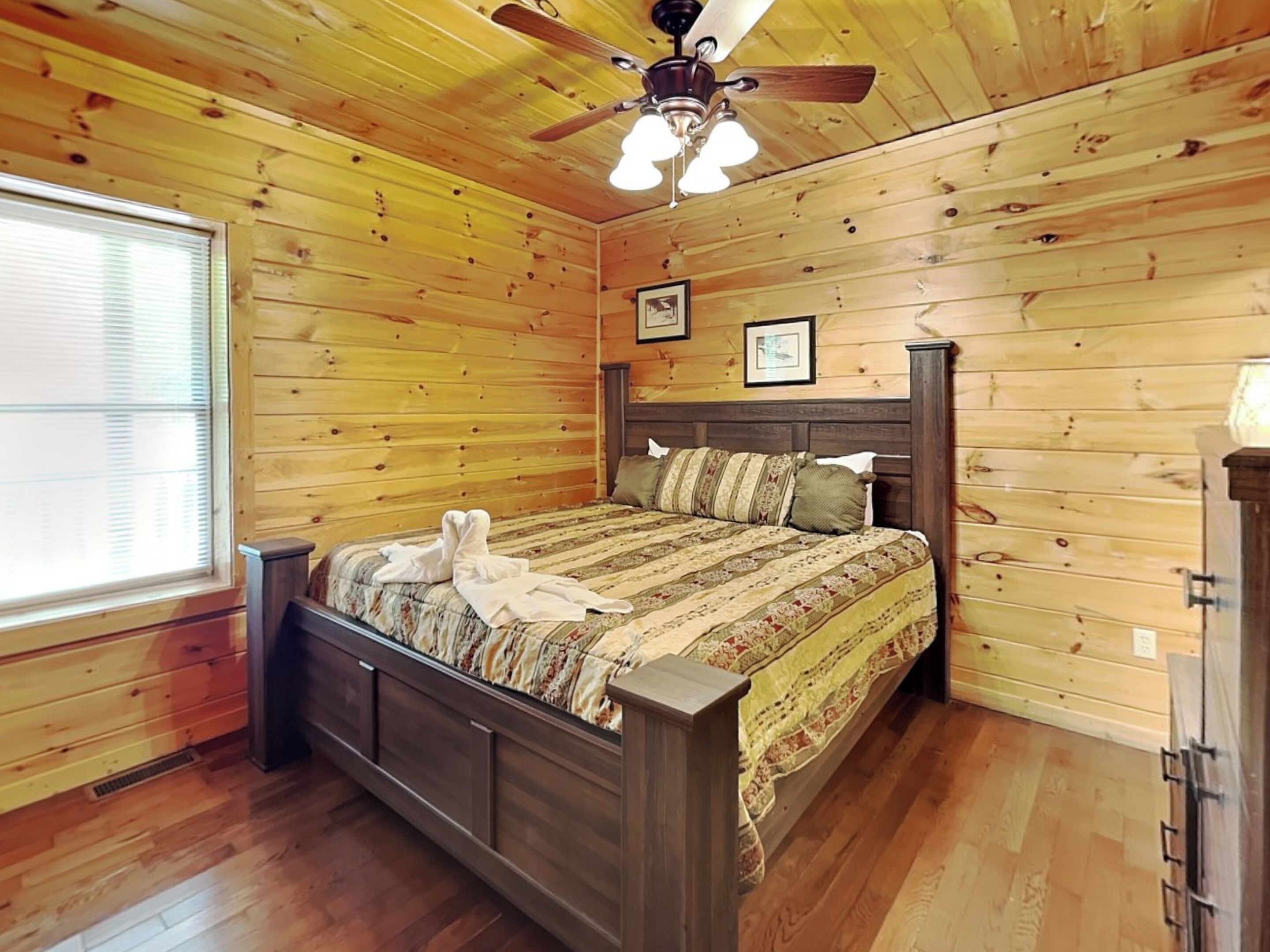 Quarto com painéis de madeira, uma cama, um ventilador de teto e uma janela.