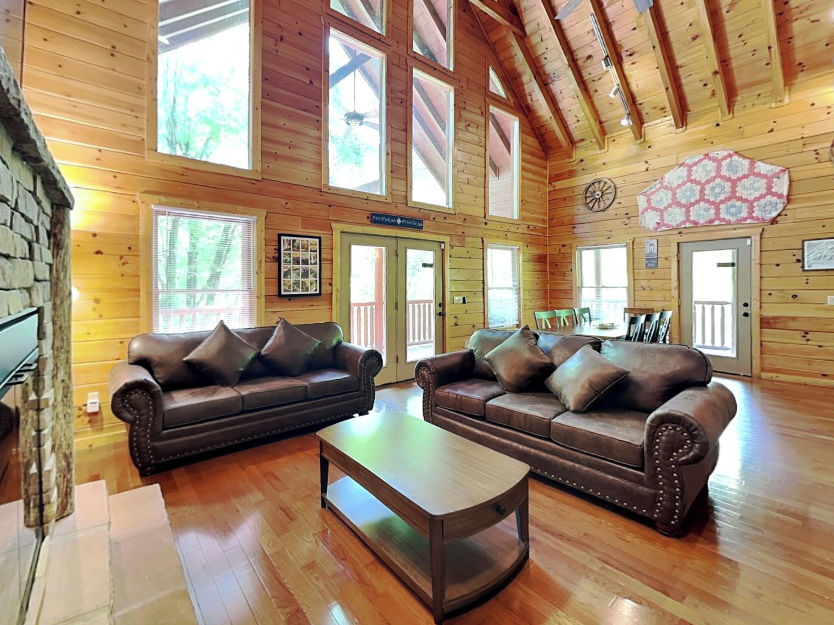 A spacious log cabin with two leather sofas, a wooden coffee table, and large windows allowing natural light.