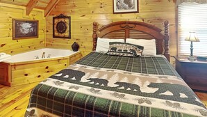 A wooden cabin bedroom with a large bed, a wooden headboard, a wooden dresser, a bathtub, and a framed picture on the wall. - Aspen's Envy by Jackson Mountain Rentals (Pigeon Forge)