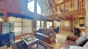 A spacious cabin interior with a high ceiling, wooden walls, a dining area, and a kitchen. - Aspen's Envy by Jackson Mountain Rentals (Pigeon Forge)