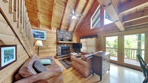 A cozy cabin interior with wooden walls, a stone fireplace, leather sofas, and a TV. - Aspen's Envy by Jackson Mountain Rentals (Pigeon Forge)